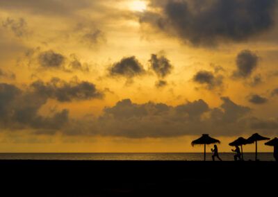 playa, atardecer, siluetas, personas, sombrillas, mar, cielo dorado, nubes, costa, verano, vacaciones, horizonte, luz cálida, paisaje marino, ocio, arena, exterior, calma, crepúsculo, fotografía de viaje.