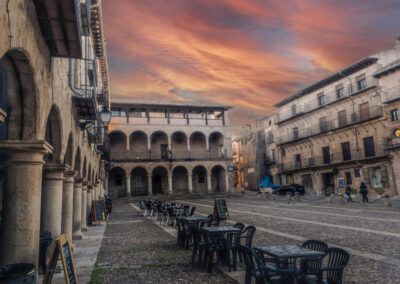 plaza histórica, soportales, atardecer, cielo anaranjado, arquitectura tradicional, terrazas, adoquines, casco antiguo, patrimonio, turismo, pueblo, columnas, edificios antiguos, paisaje urbano, España.