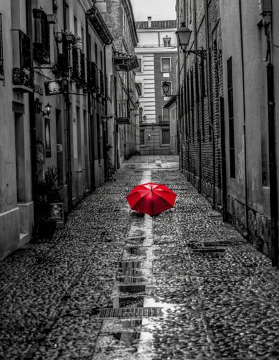paraguas rojo, blanco y negro, color selectivo, calle empedrada, lluvia, reflejos, soledad, contraste, casco histórico, fotografía artística, adoquines mojados, calle vacía, melancolía, composición urbana, arquitectura.