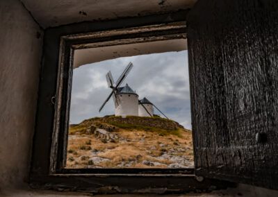 molinos de viento, ventana, marco natural, arquitectura tradicional, Castilla-La Mancha, Consuegra, paisaje manchego, patrimonio, madera, puerta antigua, perspectiva, turismo, España, molino, historia, cielo nublado, campo, Don Quijote, fotografía de viaje, composición creativa.