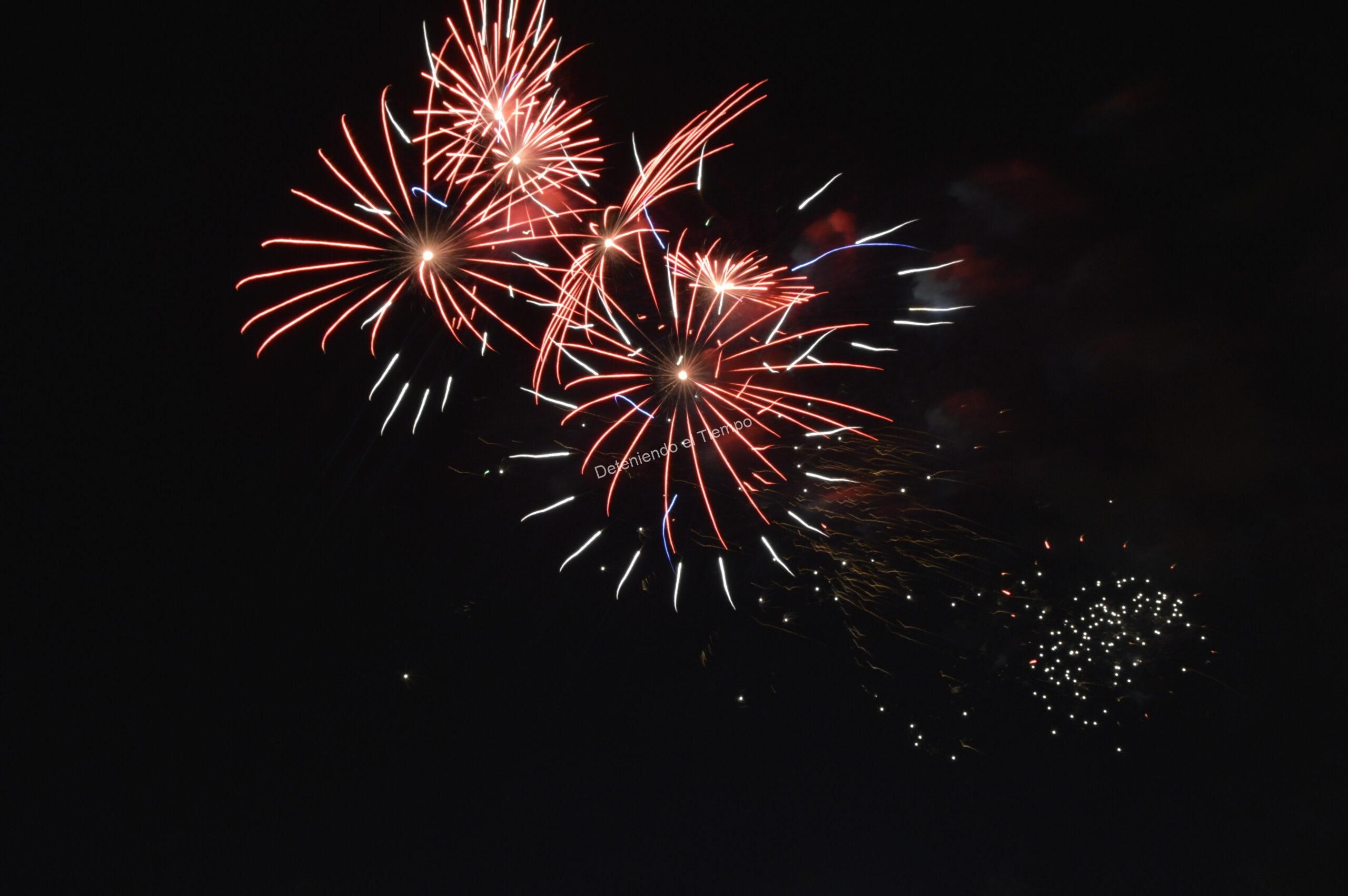 Explosión de fuegos artificiales iluminando la oscuridad con intensos destellos rojos y blancos. Una celebración visual llena de energía, movimiento y color capturada en plena noche.