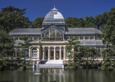 Palacio de Cristal, Madrid, parque del Retiro, arquitectura, hierro y vidrio, fachada, estanque, fuente, monumento, edificio histórico, turismo, jardín, patrimonio cultural, cielo azul, simetría.