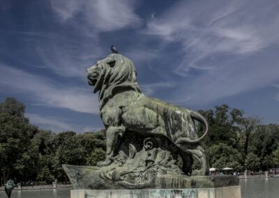 león, escultura de bronce, paloma, parque del Retiro, Madrid, estatua, monumento, arte urbano, cielo, nubes, estanque, naturaleza, patrimonio, fuerza, simbolismo.
