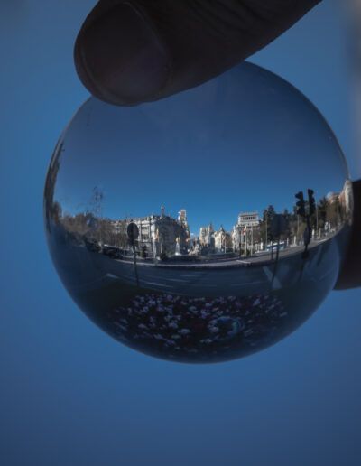 Madrid, esfera de cristal, bola de cristal, reflejo, fotografía urbana, ciudad, mano, arquitectura, paisaje urbano, perspectiva creativa, efecto óptico, cielo azul, composición fotográfica, turismo, fotografía artística.