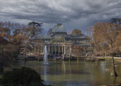 Palacio de Cristal, parque del Retiro, Madrid, otoño, cielo tormentoso, nubes, estanque, fuente, arquitectura, paisaje dramático, naturaleza, árboles, turismo, patrimonio, reflejo.