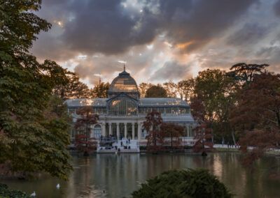 Palacio de Cristal, parque del Retiro, Madrid, arquitectura de hierro y cristal, atardecer, estanque, reflejo, otoño, jardín, naturaleza, patrimonio, turismo, cielo dramático, paisaje urbano, monumento.