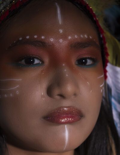 primerísimo plano, rostro, joven, maquillaje facial, pintura blanca, mirada, ojos, labios, plumas, retrato artístico, detalle, belleza, fondo oscuro, expresión, fotografía de estudio.