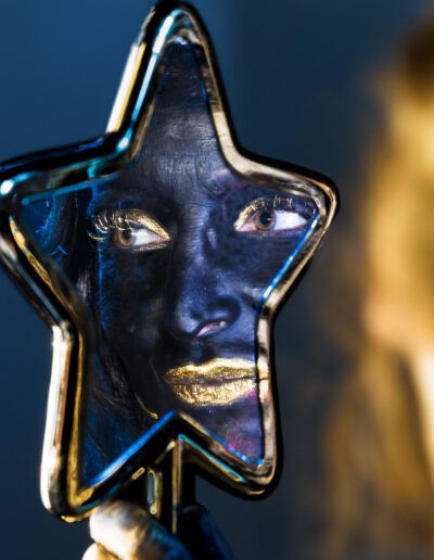 reflejo, espejo de estrella, rostro, pintura facial, maquillaje dorado, negro, ojos, primer plano, retrato conceptual, fantasía, brillo, identidad, fotografía artística, detalle, iluminación.