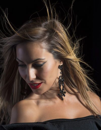 mujer, cabello al viento, vestido negro, retrato, movimiento, pendientes, glamour, moda, fondo negro, labios rojos, iluminación, dinamismo, belleza, estudio, elegancia.