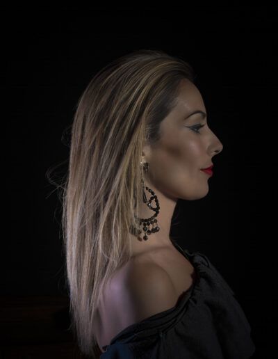 perfil, mujer, vestido negro, cabello liso, pendientes, retrato, fondo negro, elegancia, luz suave, moda, glamour, silueta, labios rojos, fotografía de estudio, belleza.