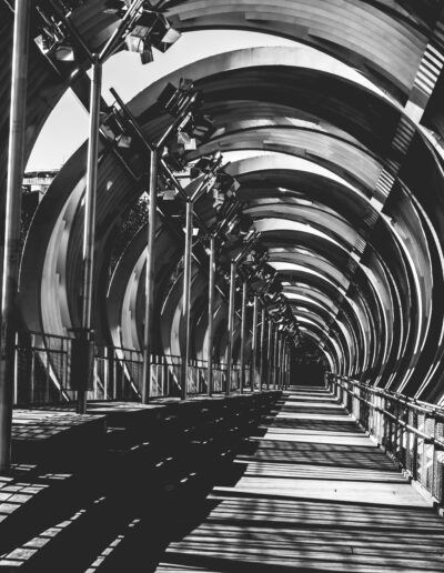 pasarela, arquitectura moderna, estructura metálica, blanco y negro, geometría, líneas, perspectiva, sombras, túnel, simetría, diseño urbano, profundidad, repetición, puente peatonal, abstracción arquitectónica.