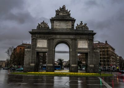 Puerta de Toledo, Madrid, lluvia, monumento, arco, calzada mojada, reflejos, tráfico, cielo gris, arquitectura histórica, glorieta, ciudad, patrimonio, ambiente lluvioso, España