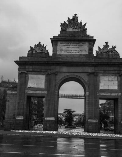 Puerta de Toledo, Madrid, monumento, lluvia, blanco y negro, arquitectura histórica, arco, calzada mojada, reflejos, glorieta, patrimonio, ciudad, cielo nublado, turismo, fotografía urbana.