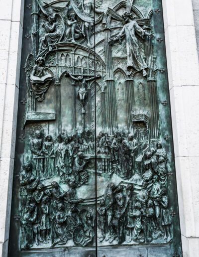 puerta de bronce, relieve, escultura, arte religioso, ángeles, escenas bíblicas, catedral, arquitectura gótica, patrimonio, metal, pátina verde, entrada monumental, iconografía cristiana, detalle artístico, Madrid.