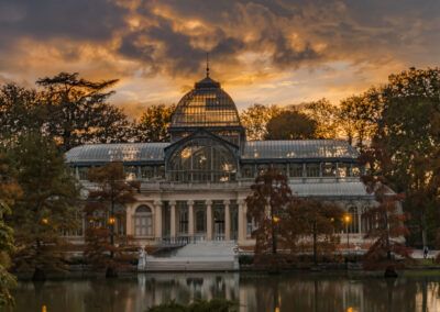 Palacio de Cristal, parque del Retiro, Madrid, atardecer, puesta de sol, cielo dorado, estanque, reflejo, arquitectura, silueta, otoño, paisaje, monumento, naturaleza, luz cálida.