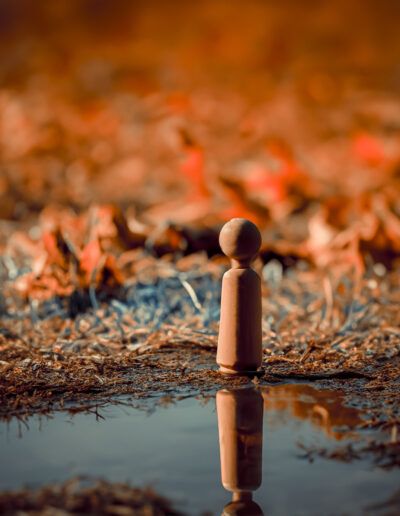 figura de madera, fuego, llamas, reflejo, charco, tonos cálidos, naranja, fotografía conceptual, soledad, contemplación, peligro, calor, contraste, paisaje abstracto, minimalismo.