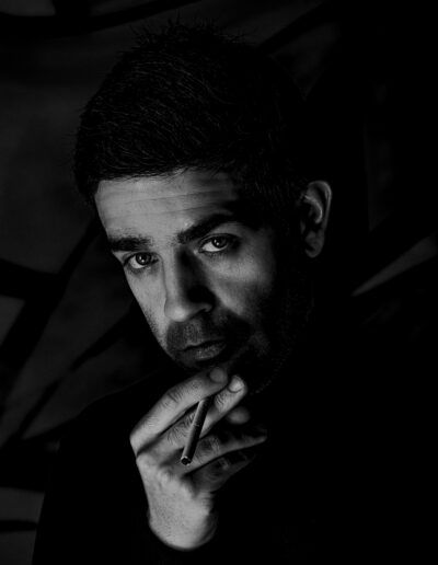 hombre, retrato, cigarro, blanco y negro, sombras, claroscuro, mirada intensa, gesto pensativo, iluminación dramática, fondo oscuro, misterio, introspección, contraste, fotografía de estudio, retrato artístico.